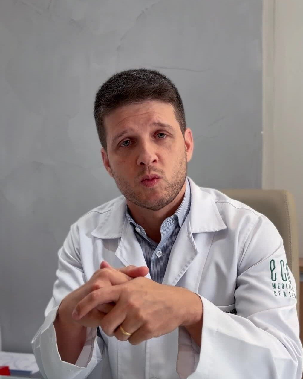 Dr. Luiz Müller Avila de jaleco, sentado no consultório, gravando um vídeo