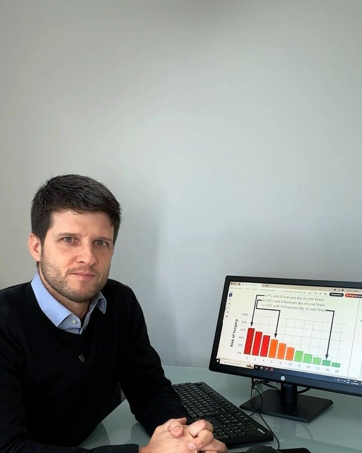 Dr. Luiz Müller Avila no consultório, ao lado de um computador com um gráfico na tela